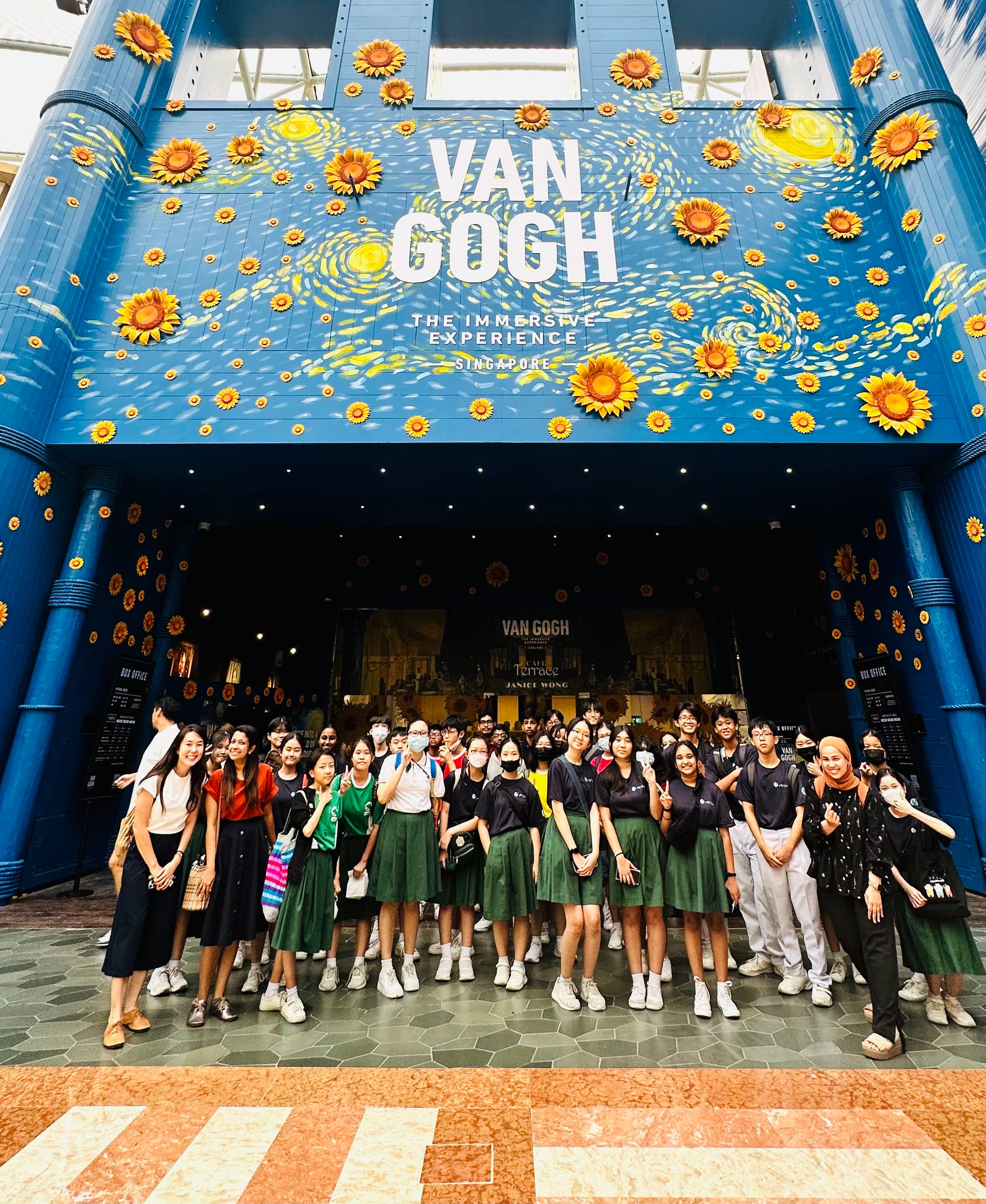 A large group poses in front of the Van Gogh The Immersive Experience Singapore entrance decorated with sunflowers.